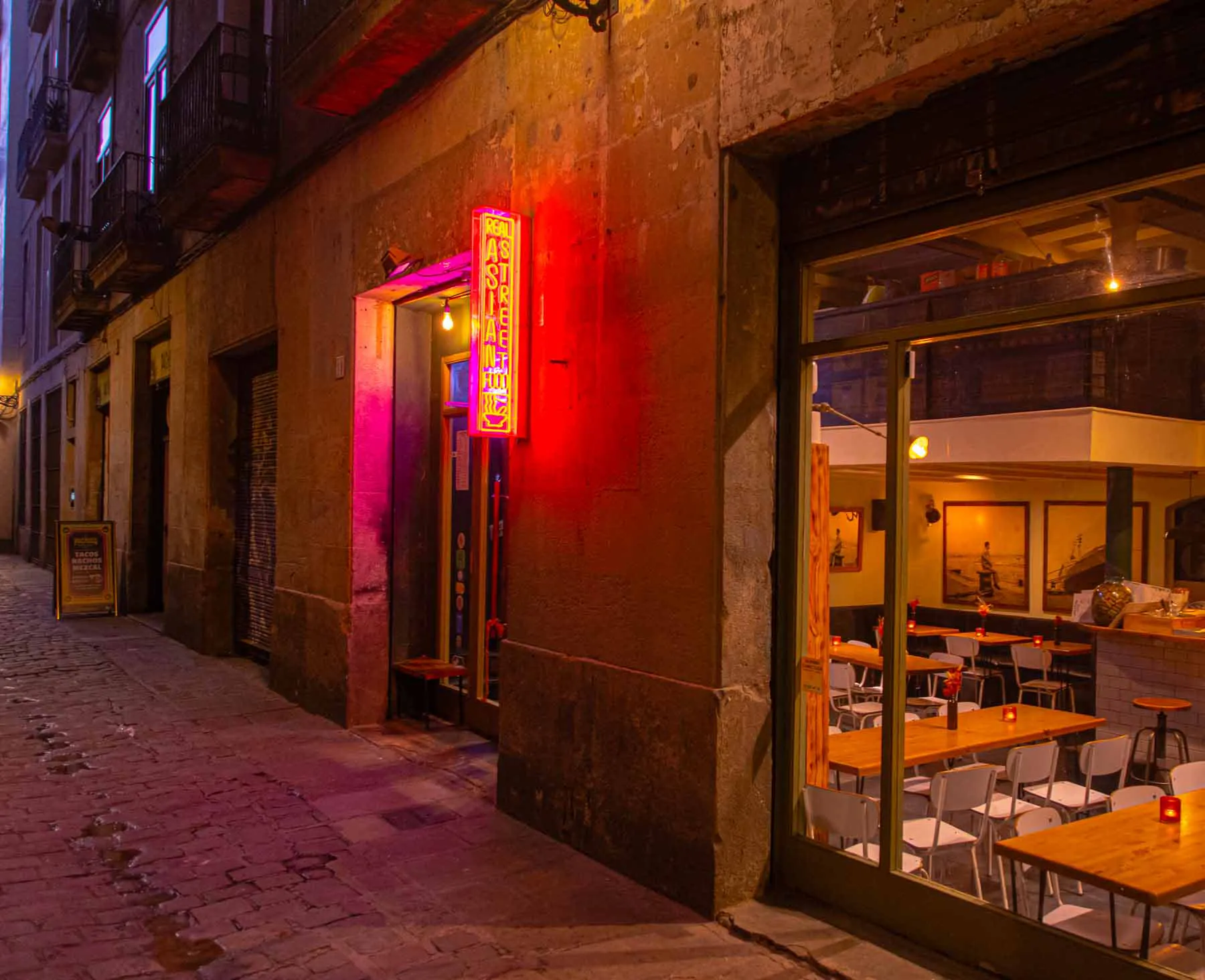 The lane outside Koku Kitchen El Gòtic, with its red neon sign and the dining room through the window