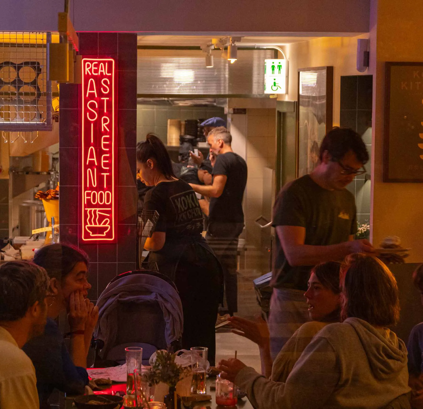 The red REAL ASIAN STREET FOOD neon over a busy evening at Koku Kitchen Sant Antoni