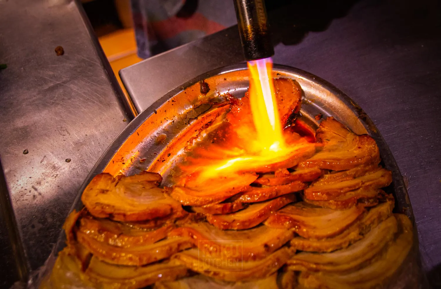 Chashu pork being seared with a blowtorch in the kitchen of Koku Kitchen El Born