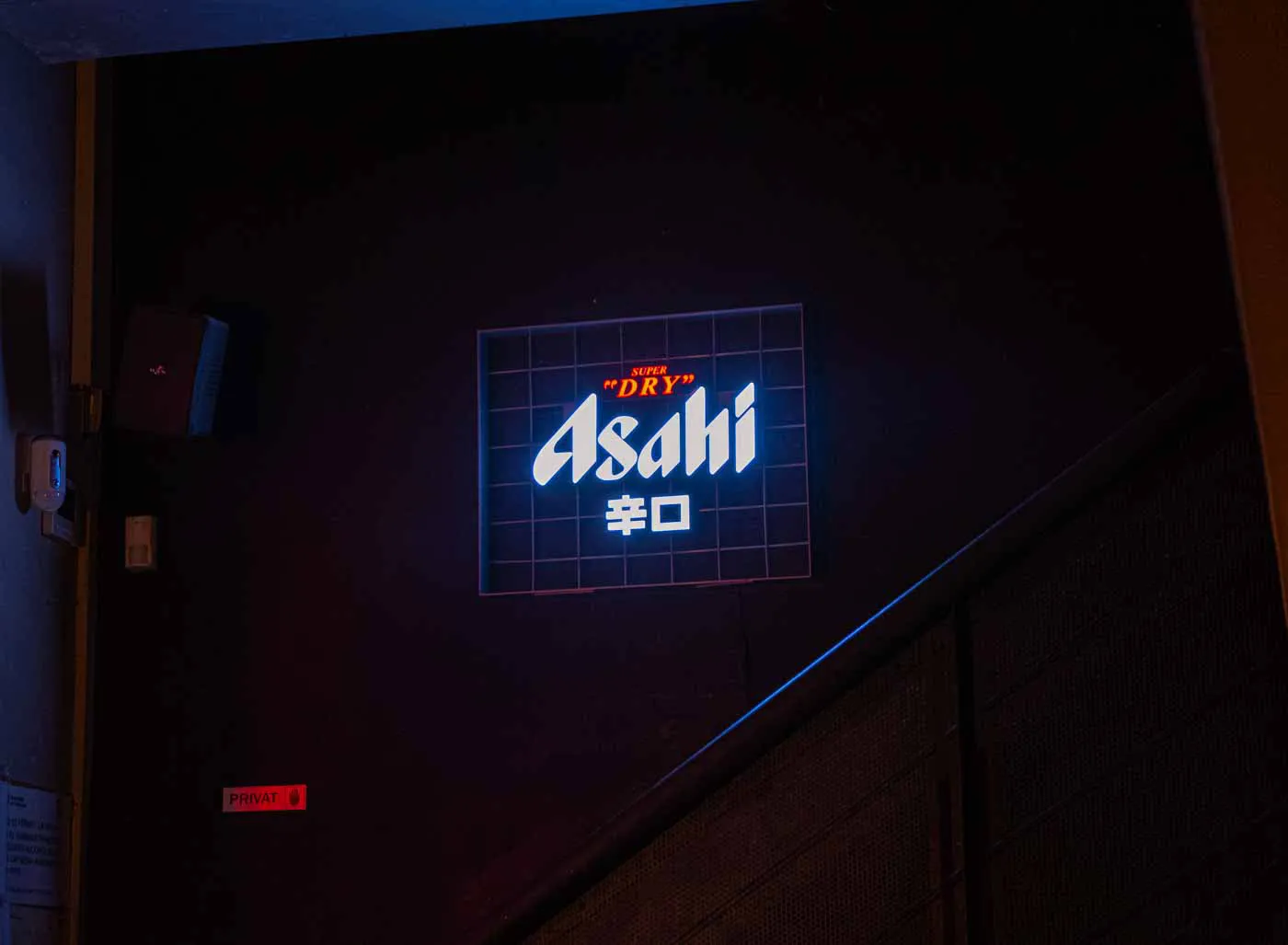 An Asahi neon sign on a dark wall at Koku Kitchen El Gòtic